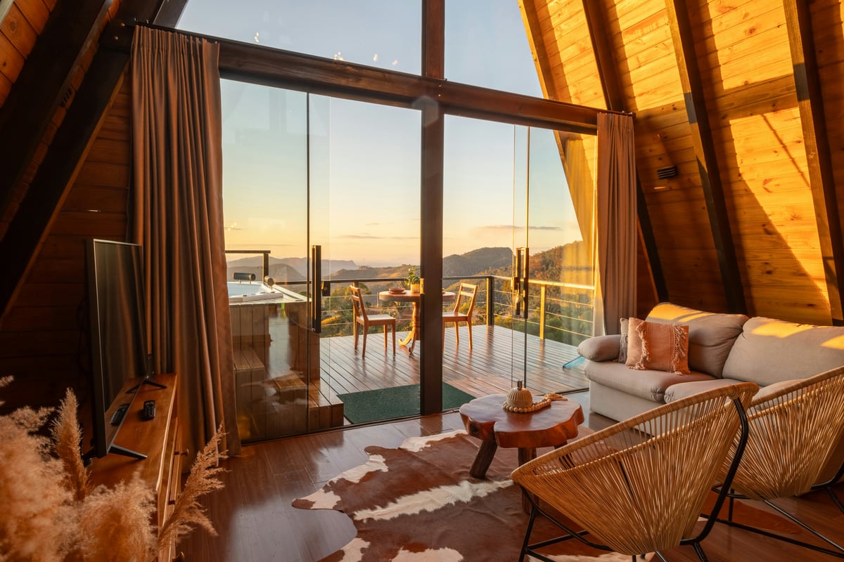 A warm timber cabin interior opening to a mountain deck at golden hour