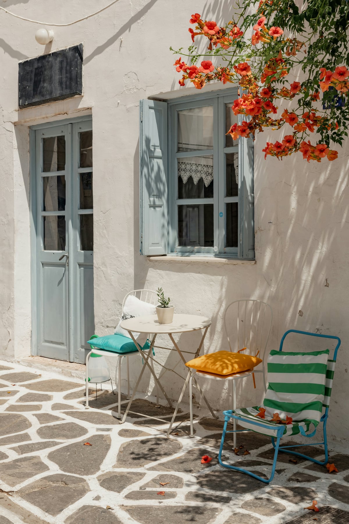 A sunlit whitewashed courtyard with pale blue shutters and orange flowers